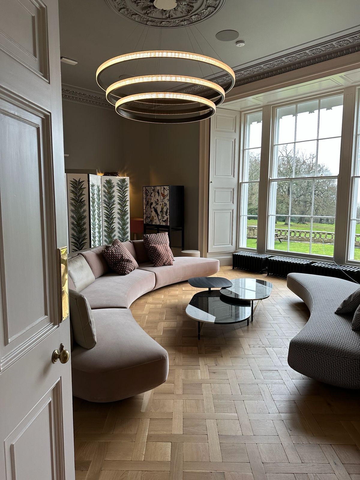 The Estate — formal living room with curved seating, ring chandeliers and garden windows