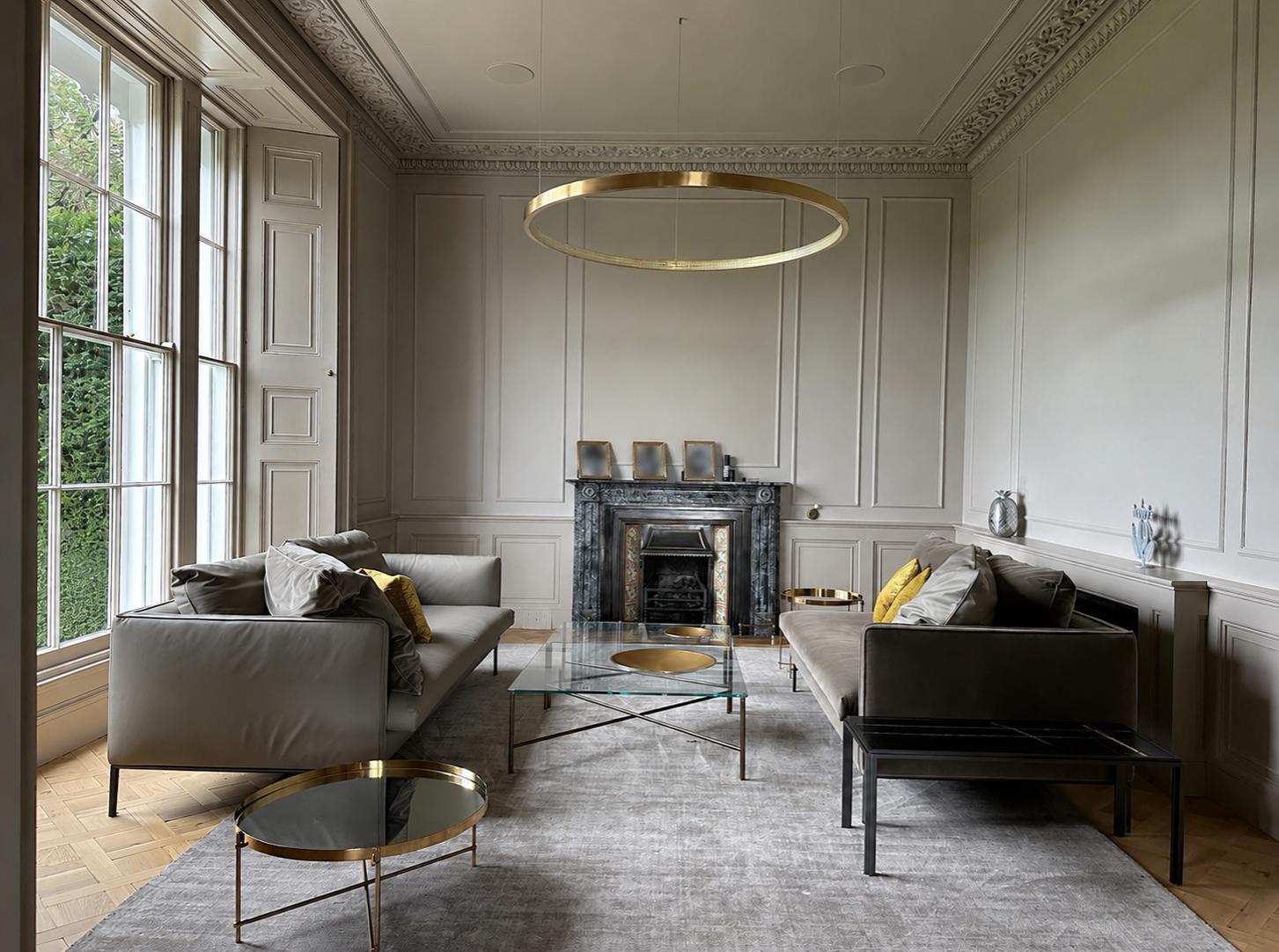 The Estate — formal drawing room with grey sofas, marble fireplace and brass ring chandelier